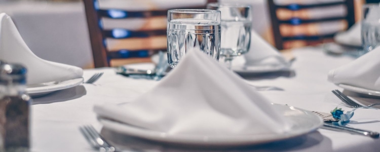 dinner places set with cutlery and water glasses; folded white napkins sit on top of the plates
