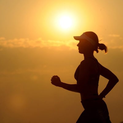 silhouette of woman running at dusk or dawn; she is wearing a hat with a brim