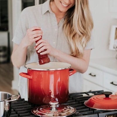 woman cooking fall recipes in kitchen; she is adding salt to a red ombre pot in a mostly white kitchen