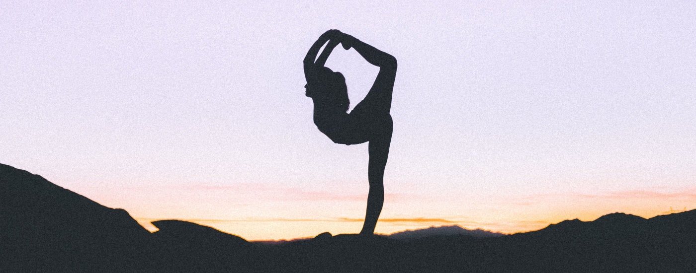 woman does yoga at sunset; she is holding an advanced yoga pose