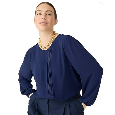 A woman wearing a dark blue top and navy pants with a gold necklace