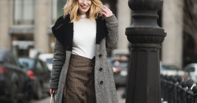 stylish young professional woman walking down a city street wearing a coat and sweater